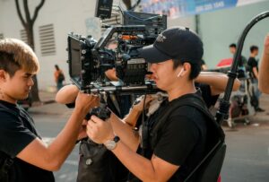 Two people operate a shoulder-mounted camera on a movie set