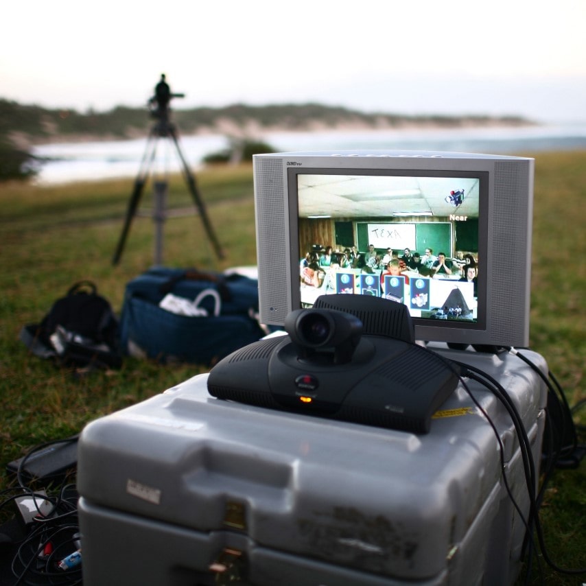 A videoconference setup outdoors, with a screen showing participants at another location