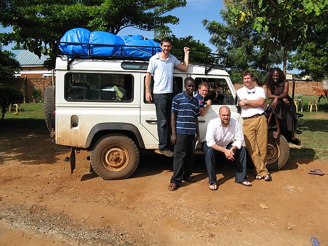 The four GNG founders and several locals pose before a white SUV laiden with equipment in an African village