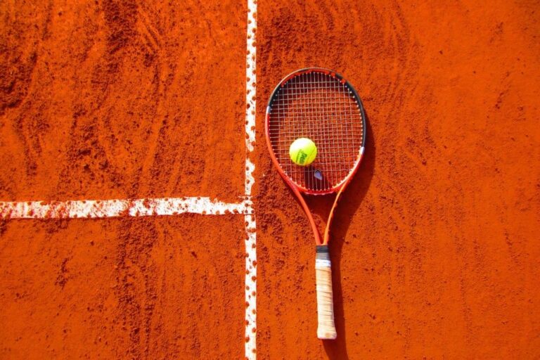 A tennis racket and a ball resting on a red surface.