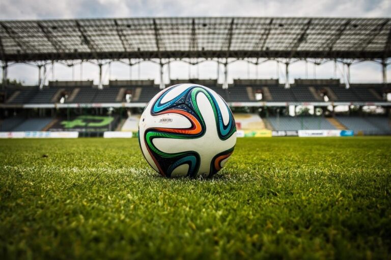 A soccer ball resting on astroturf in a stadium.