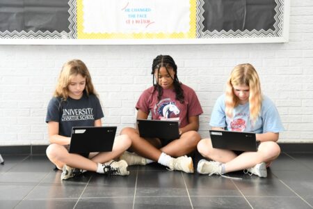 Three University Charter School students sit on the floor with their laptop computers